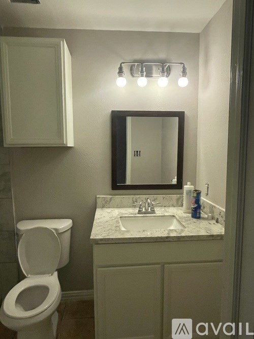 A bathroom with a toilet, sink, mirror, and lights.