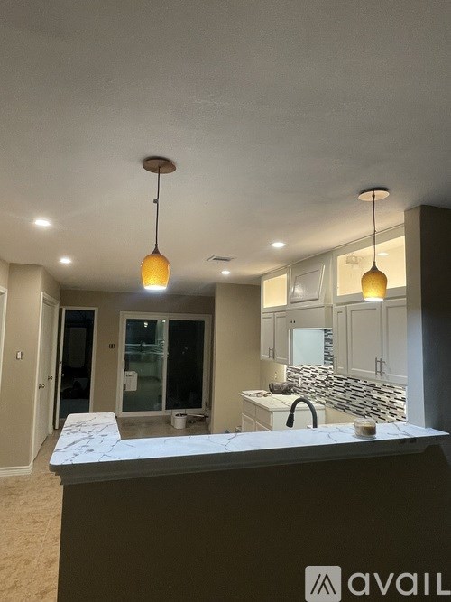 A kitchen with a marble countertop and pendant lights.