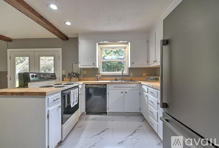 A kitchen with white cabinets and appliances, a marble floor, and a window with a view of trees.