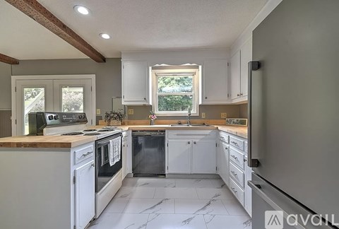 A kitchen with white cabinets and appliances, a marble floor, and a window with a view of trees.