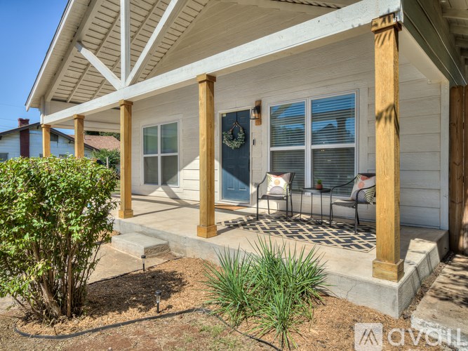 A white house with a porch and a green bush.