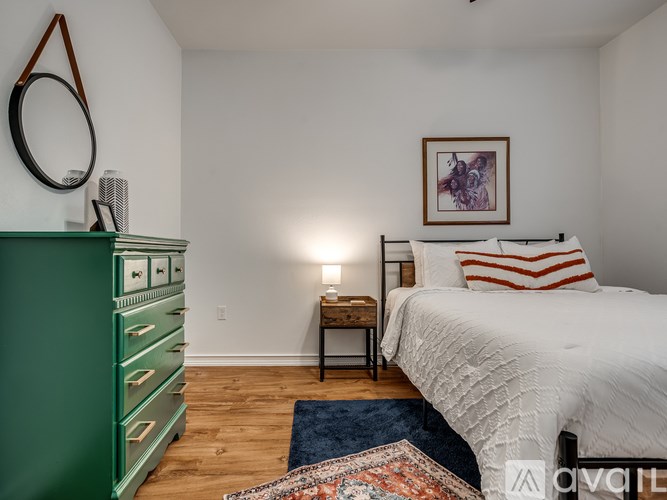 A bedroom with a white bed, green dresser, and a wooden table with a lamp on it.