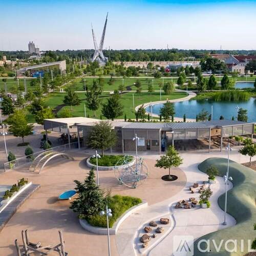 A park with a playground, a pond, and a tall sculpture in the distance.