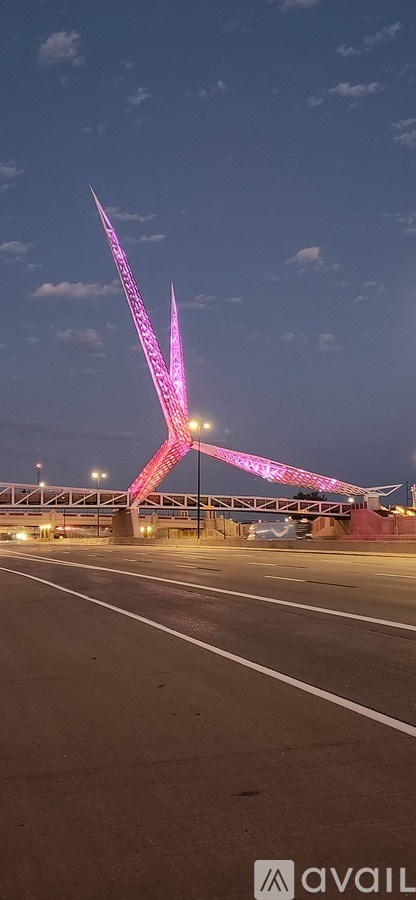 A tall structure with a unique design is illuminated in pink and purple lights.