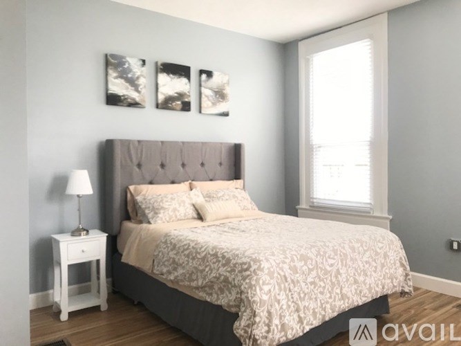 A bedroom with a large bed and a small table with a lamp.