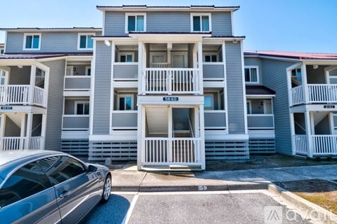 A silver car is parked in front of a grey apartment building.