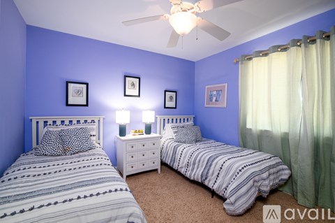A bedroom with two beds, one with a white headboard and the other with a striped comforter.