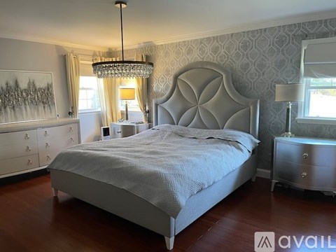 A bedroom with a large bed, a chandelier, and a dresser with a mirror.