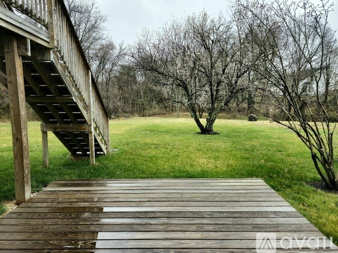 A wooden deck leads to a staircase in a grassy field.