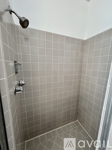 A shower with a grey tile wall and a silver shower head.