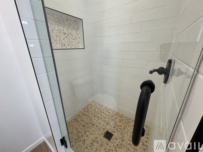 A bathroom with a glass shower door and a black handle.