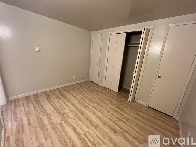 A room with light wood flooring and white walls, with a door open to another room.