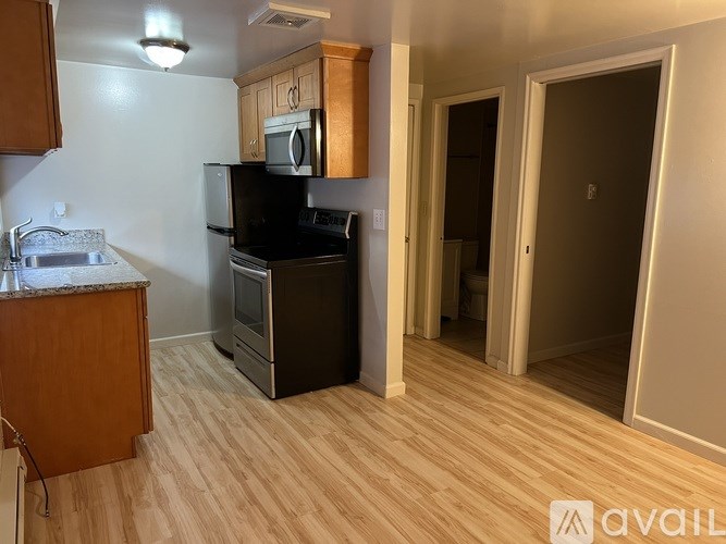 A kitchen with a black fridge and stove, a microwave above the stove, and wooden flooring.