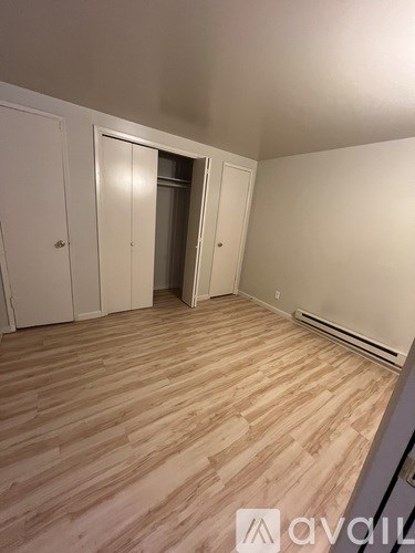 A room with wooden flooring and white walls, with a door open to another room.
