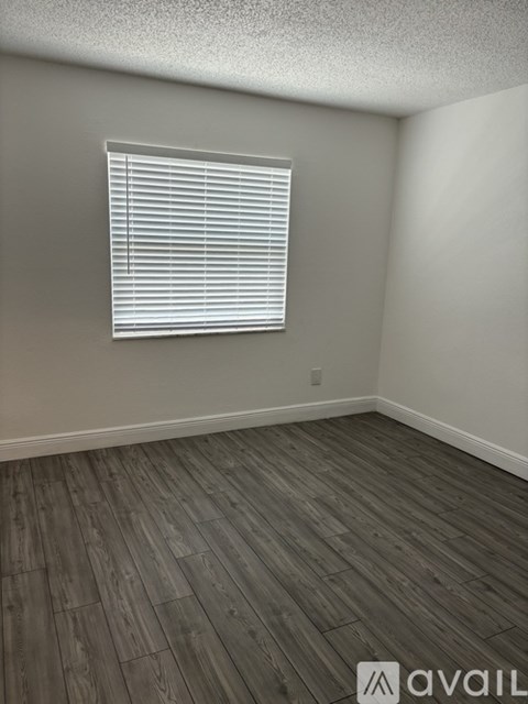 A room with wooden flooring and a window with blinds.
