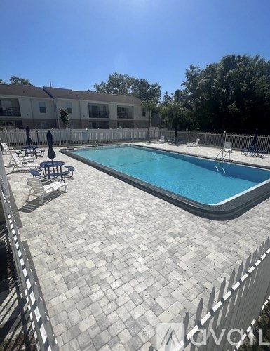 A swimming pool surrounded by a white fence and a brick patio.