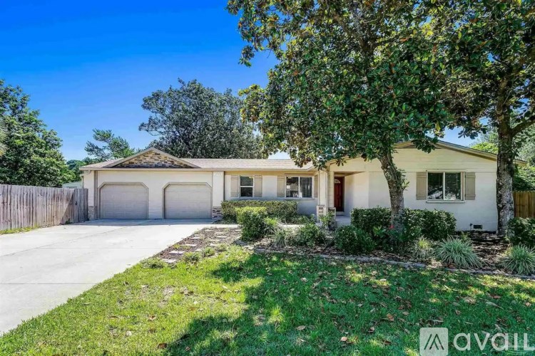 A house with a brown roof and a white garage door is surrounded by greenery.