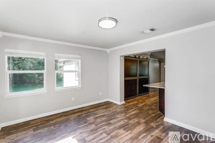 A room with wooden floors and white walls, featuring a window, a door, and a refrigerator.