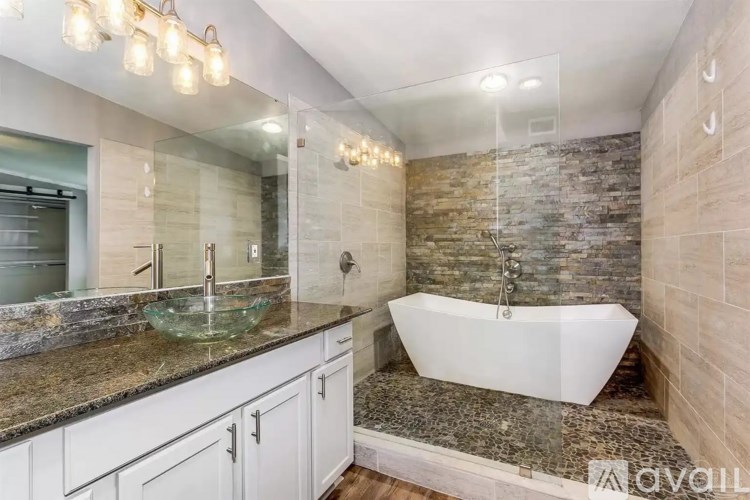 A modern bathroom with a stone wall and a white bathtub.