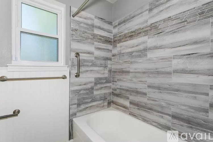 A bathroom with a marble tile wall and a white bathtub.