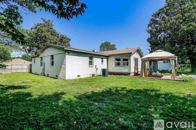 A house with a white exterior is surrounded by greenery and has a gazebo-like structure attached to it.