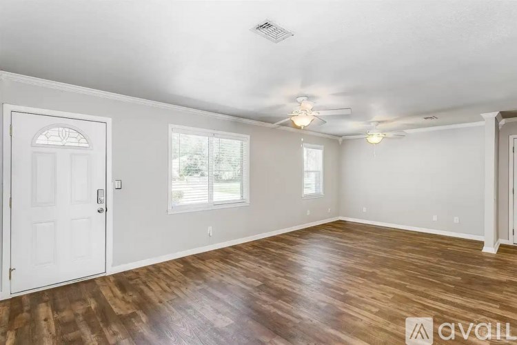 A room with wooden floors and white walls, with a ceiling fan and a door.
