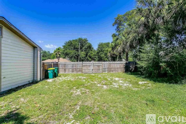 A backyard with a fence, a shed, and a green trash can.