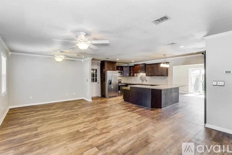 A spacious living room with a kitchen in the background and hardwood floors.