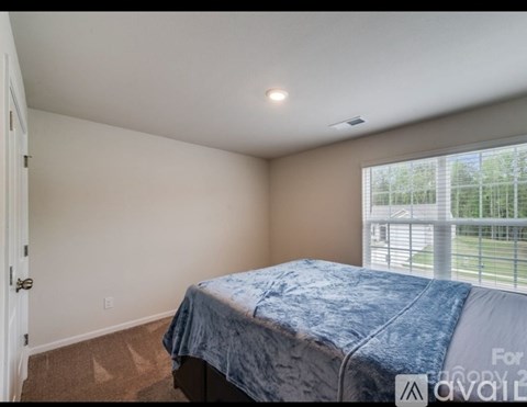 A bedroom with a bed and a window overlooking a fence.