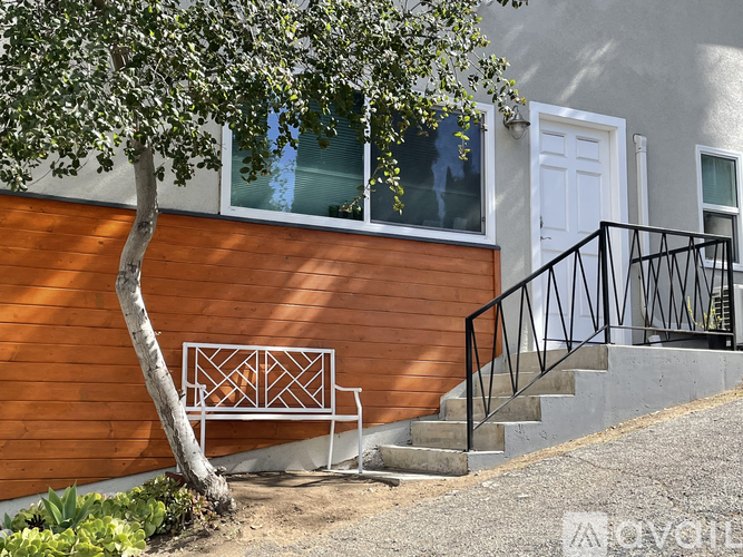 A tree in front of a wooden building with a white door and a metal railing.