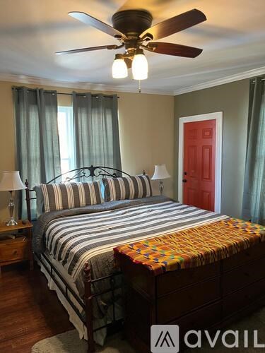 A bedroom with a bed, a ceiling fan, and a red door.