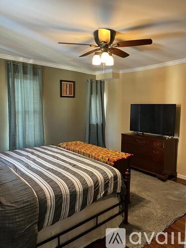 A bedroom with a bed, a television, and a ceiling fan.