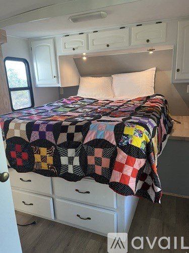 A bed with a patchwork quilt and white pillows in a room with white walls and a window.