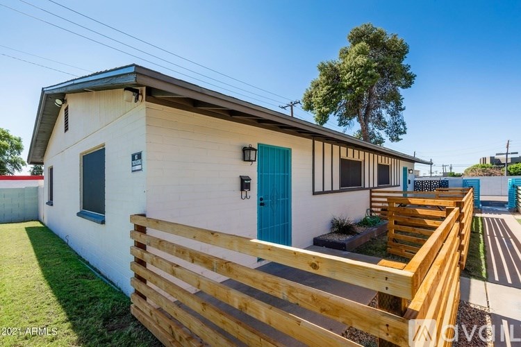 A small white house with a blue door and a wooden fence in front.