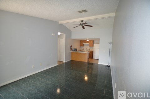A room with a ceiling fan and a kitchenette in the background.
