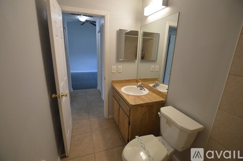 A bathroom with a toilet, sink, mirror, and a door leading to a bedroom.