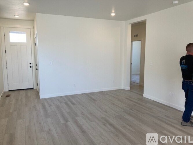 A man is standing in a room with white walls and wooden flooring.