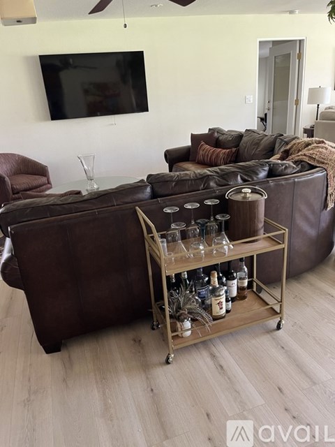 A living room with a brown leather couch and a metal cart with bottles on it.