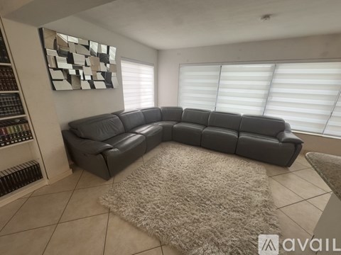 A black leather sectional sofa in a living room with a rug and a wall art.