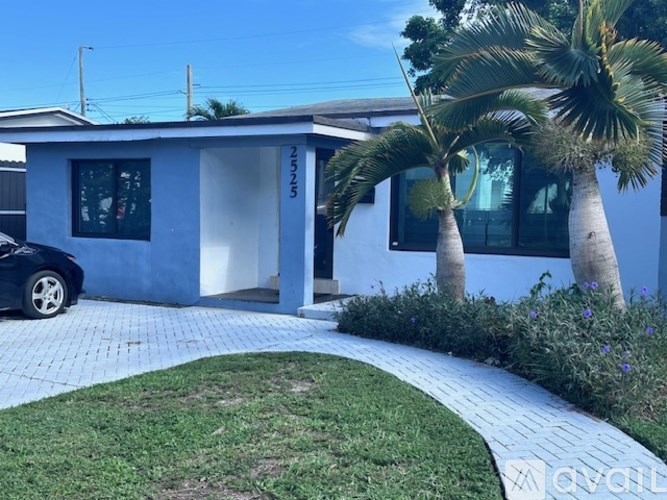 A blue house with a car parked in front and two palm trees beside it.