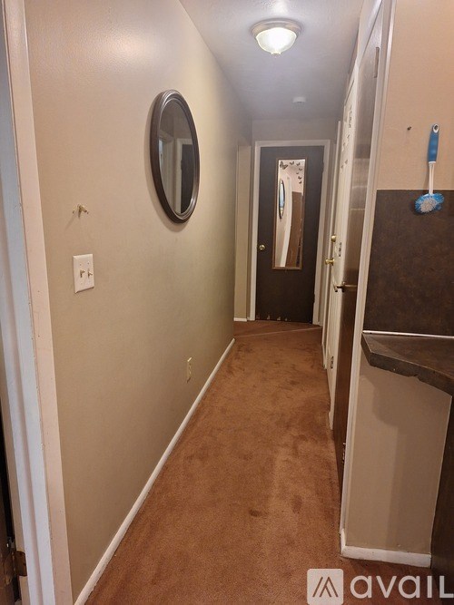 A hallway with a brown carpet and a round mirror on the wall.