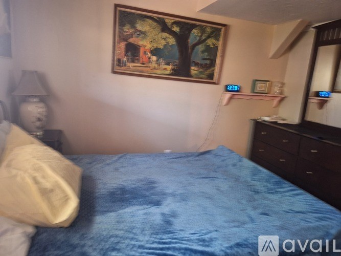 A bedroom with a blue bedspread and a painting on the wall.