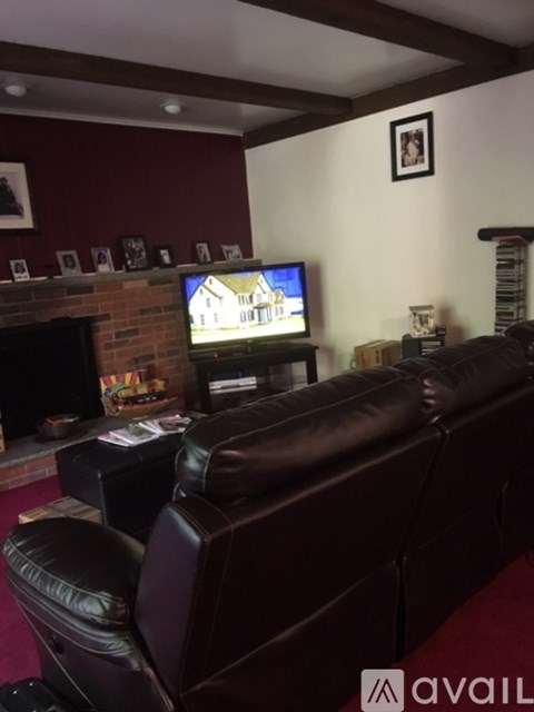 A living room with a brown leather couch and a television on a brick wall.