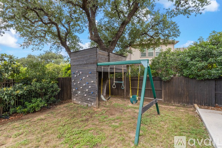 A backyard with a wooden swing set and a large tree.
