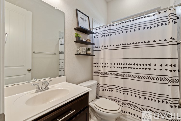 A bathroom with a sink, toilet, and a shower curtain with black triangles.