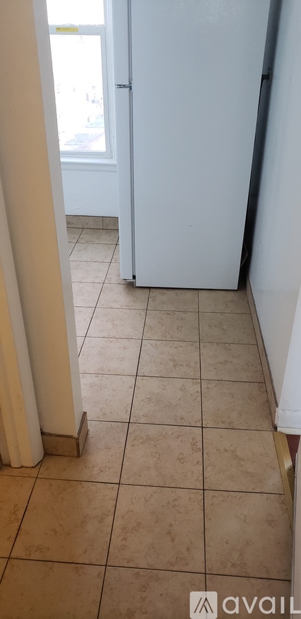 A white refrigerator in a kitchen with beige tiled flooring.