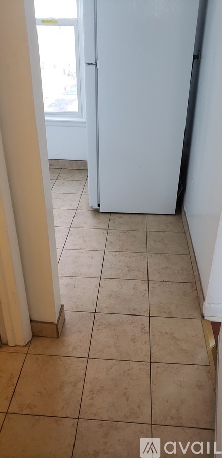 A white refrigerator in a kitchen with beige tiled flooring.