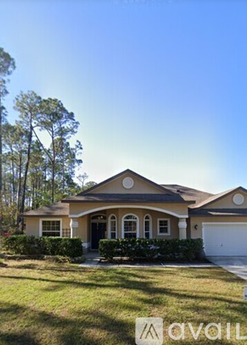 A house with a brown roof and a white garage door is surrounded by greenery.