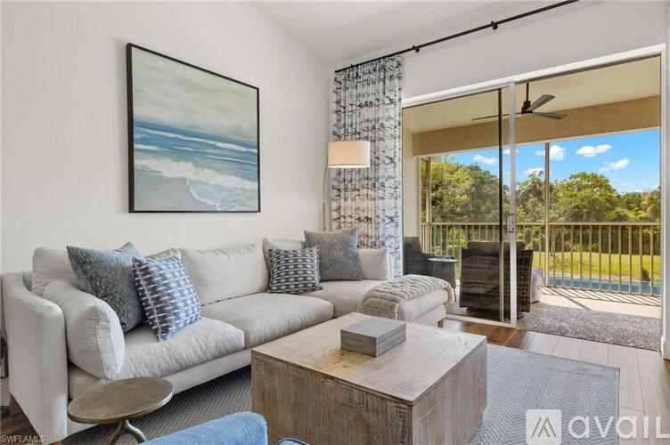 A living room with a large painting, a grey sofa, a coffee table, and a sliding glass door leading to a balcony.