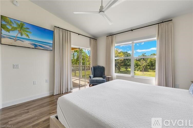 A bedroom with a large bed, a ceiling fan, and a painting of a beach scene on the wall.